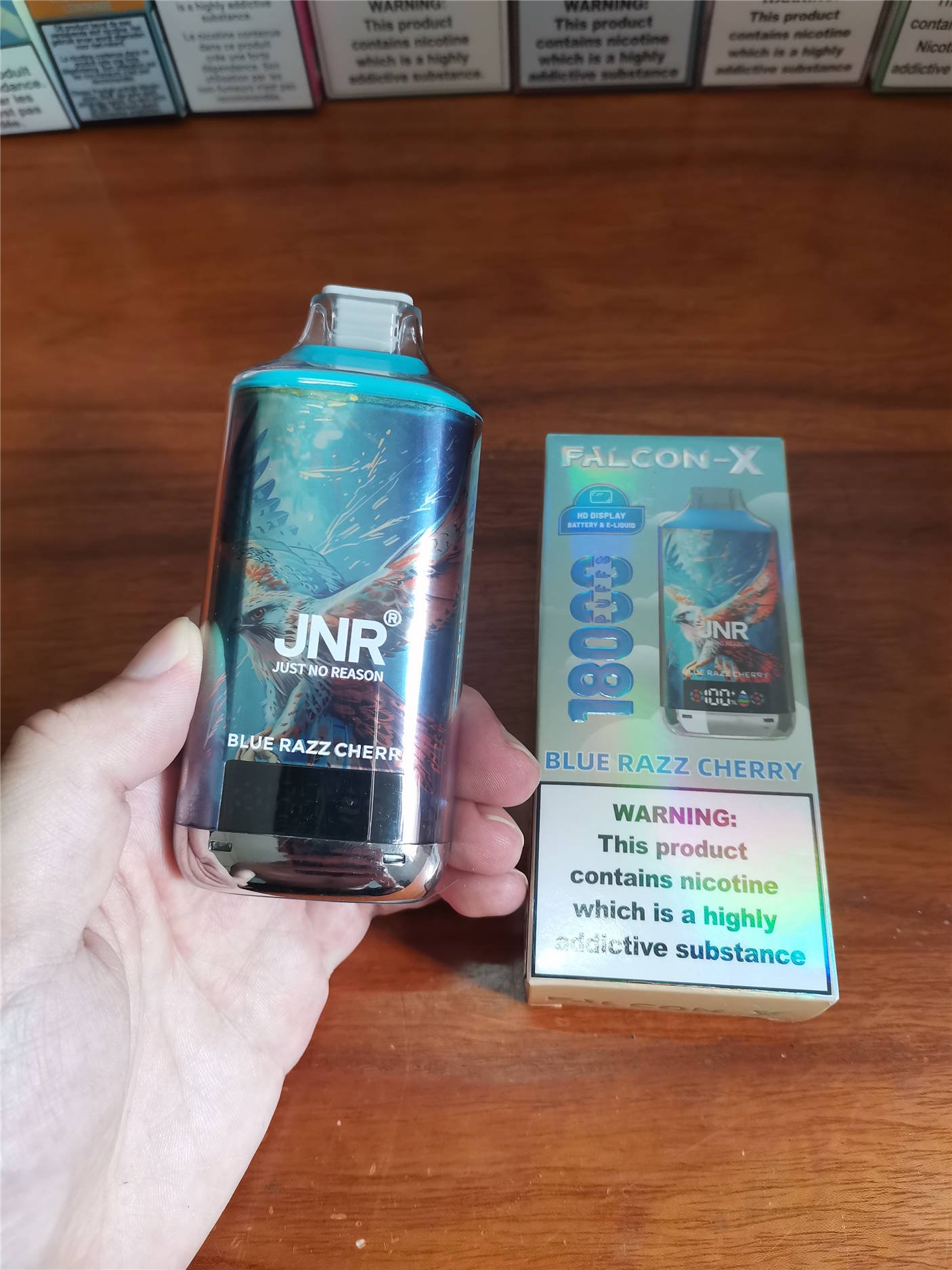 a hand holding the jnr falcon x 18k device next to the front of its original packaging box